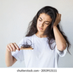 Woman looking at hairbrush with broken hair, showing symptoms of hair breakage.